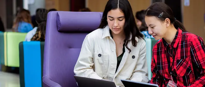 Two Carnegie Mellon students sitting in Tepper Quad, working on their laptops.