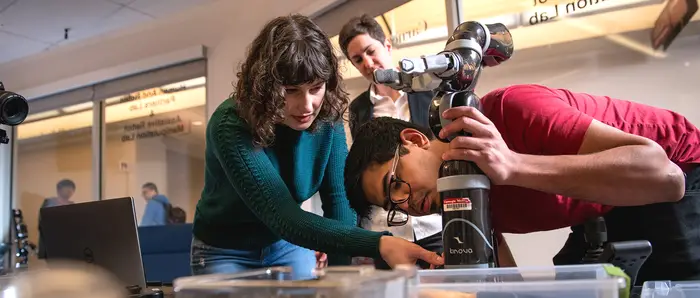 Two students working on a robot arm with their professor.